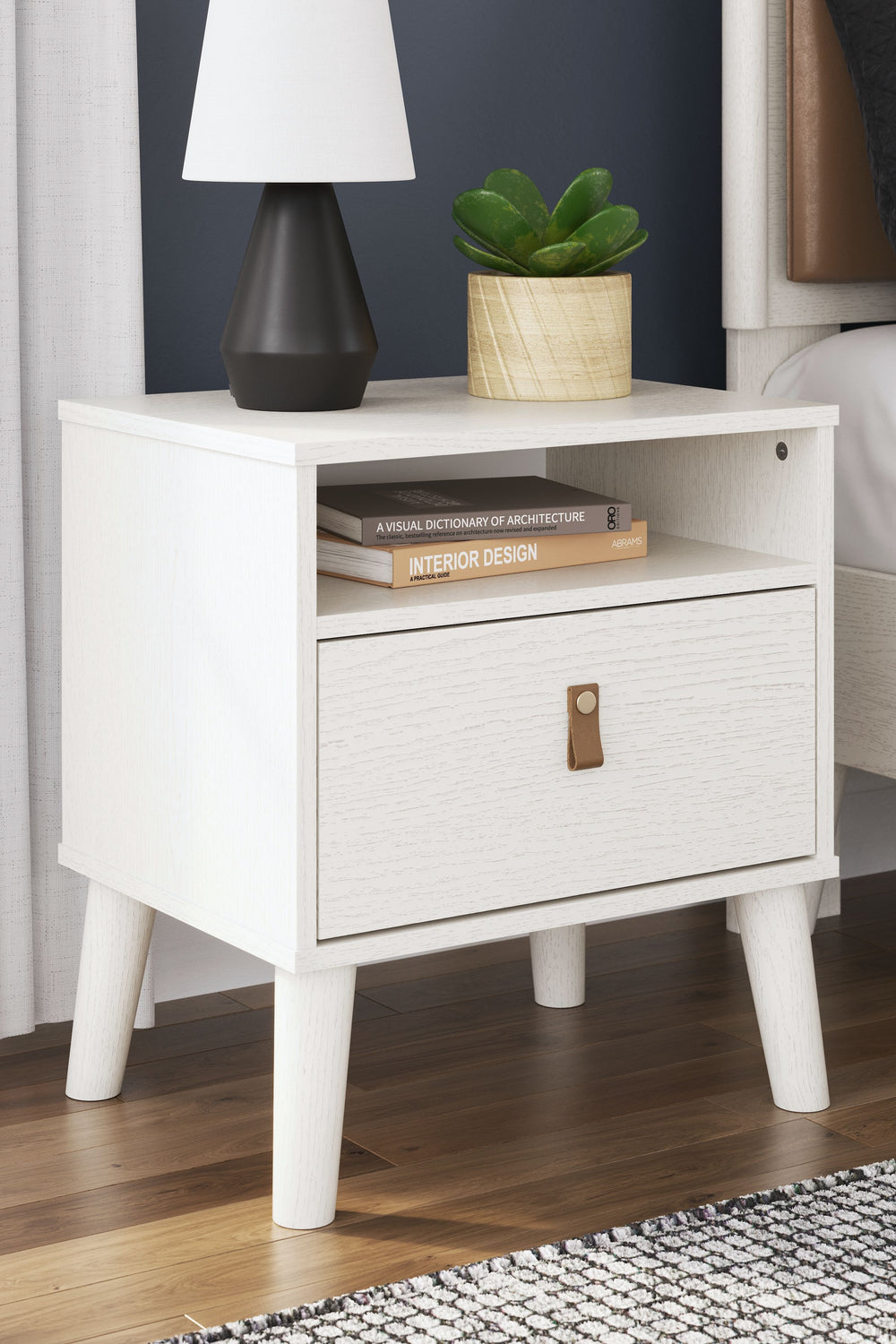 Dare to take minimalism to the max. This nightstand has an air of sleek simplicity thanks to its white painted finish with subtle replicated wood grain. Magnificently mod splay legs are a compelling complement to the streamlined design. And with two diffe