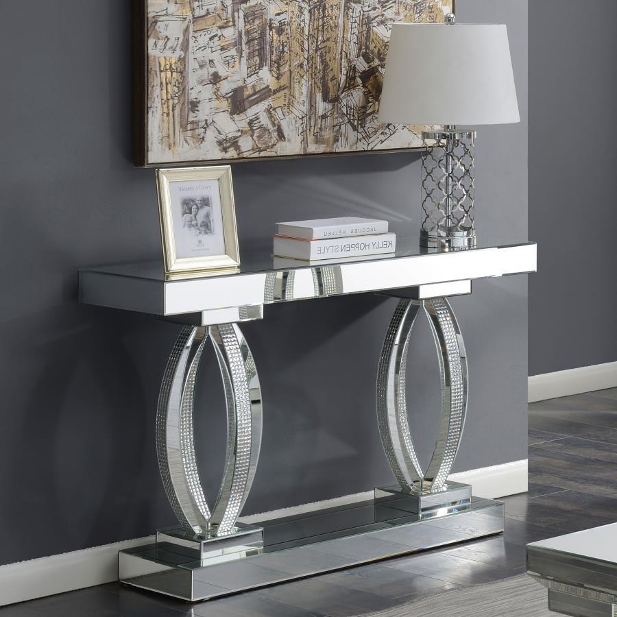 This mirrored console table features an elegant design with a rectangular top and bold, oval-shaped bases. The base is adorned with acrylic crystals, adding a luxurious and glamorous touch to its modern aesthetic. Crafted with mirrored surfaces, this tabl