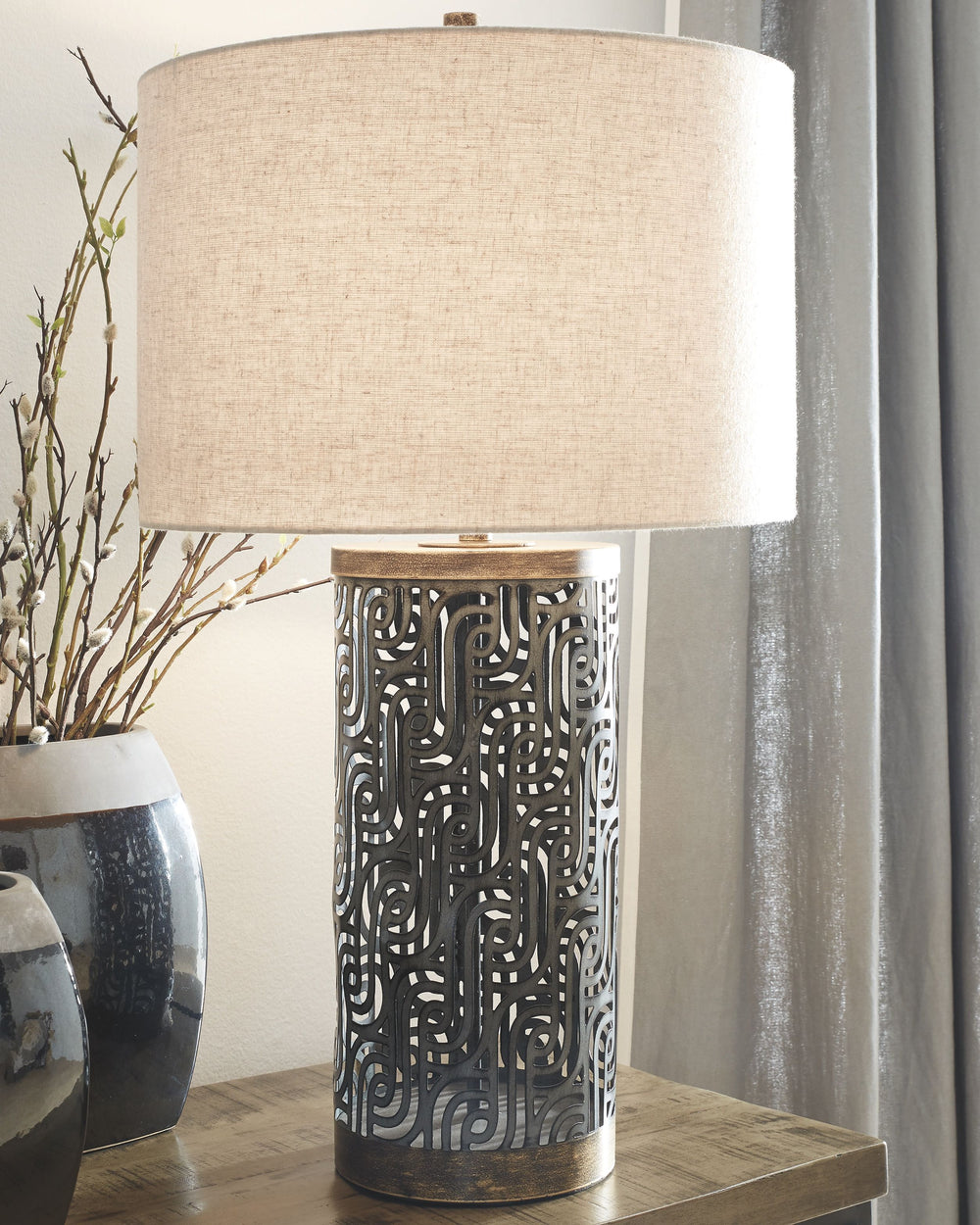 The open concept swirls of this table lamp bring presence and intrigue to any room. Antique gray and gold finished metal contrast beautifully against the light drum shade. Surely, this is contemporary style fully realized.<br><br><b>Additional Dimensions<