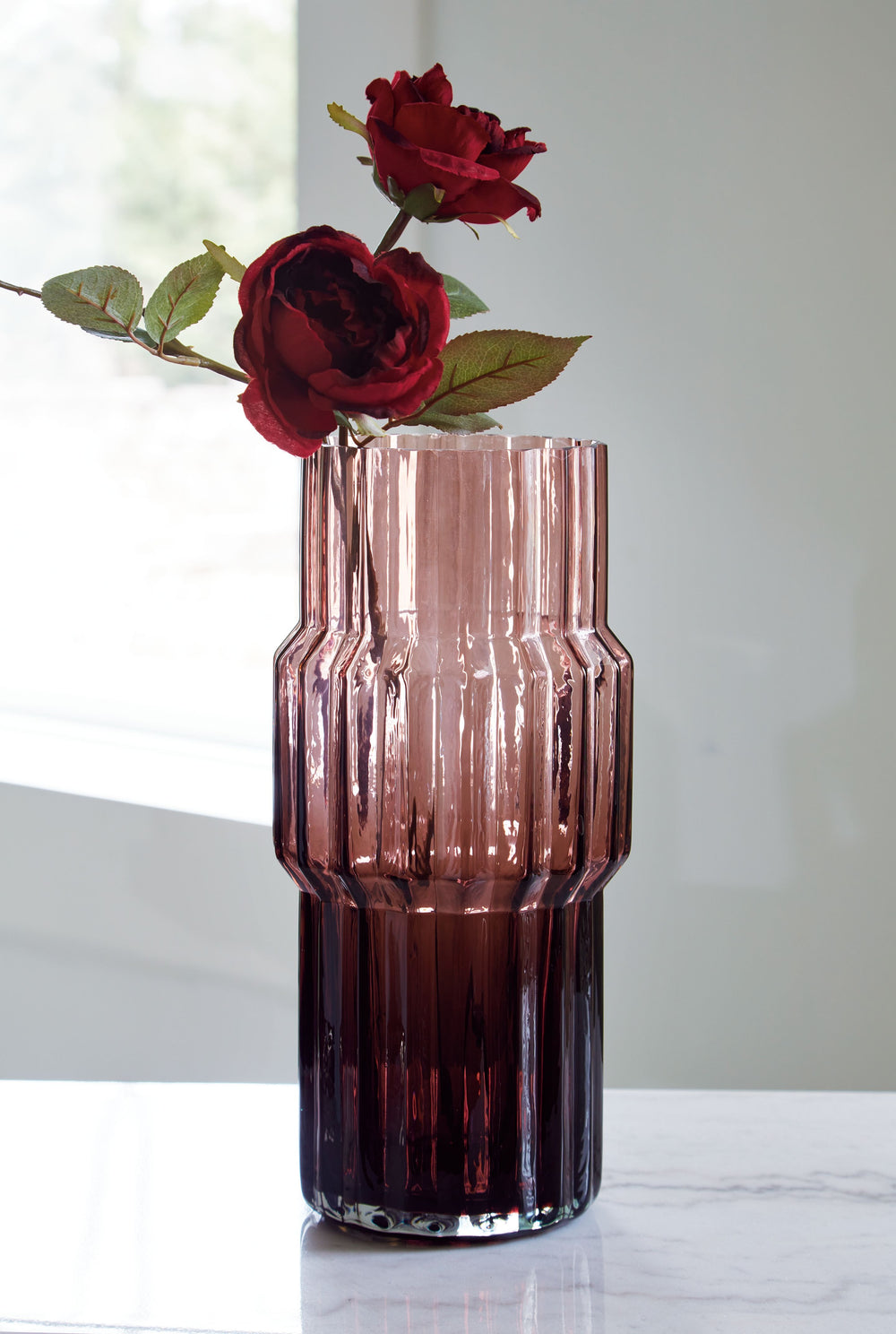 This vase, made of dark mauve-tinted glass, adds a captivating touch to indoor or outdoor decor. Its unique textured shape with oversized fluted detail creates an elegant art piece. Whether it-'s accentuating flowers or candlelight, this vase is simply st