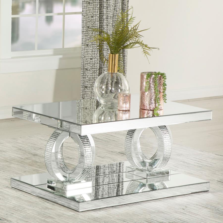 This glamorous mirrored coffee table captures the opulent spirit of Hollywood Regency design. Its base features interconnected dual rings adorned with dazzling acrylic crystals, while mirrored surfaces and softly beveled edges amplify its refined aestheti
