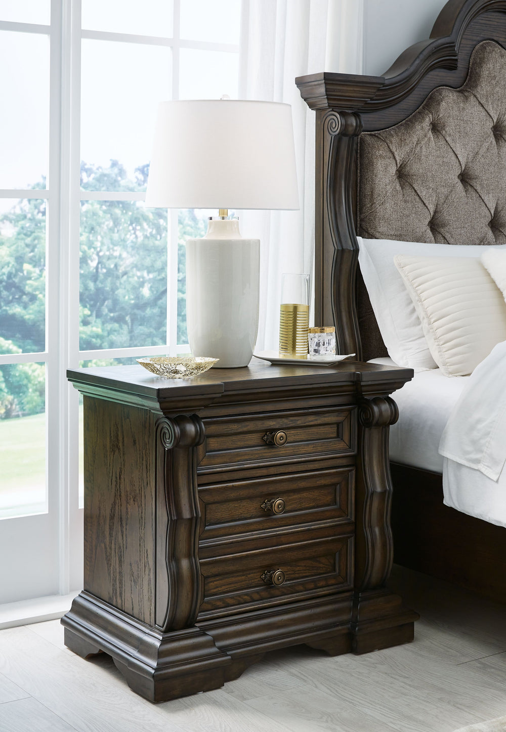 From its ornamental appliques to its large scale, this nightstand makes a bold statement. Spacious drawers store your bedtime essentials in stunning style. A hidden pull-out tray behind the bottom drawer puts your small valuables out of sight. The look is