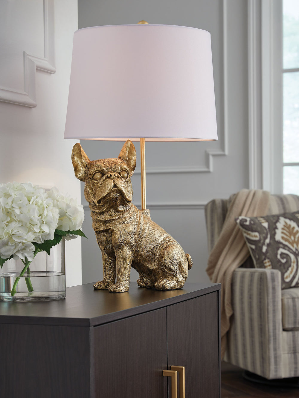 This charming table lamp brings a touch of playful sophistication to your home. An adorable French bulldog base, finished in a sleek goldtone, is sure to be a conversation starter. This lamp-'s warm and inviting ambiance makes it a delightful addition to 
