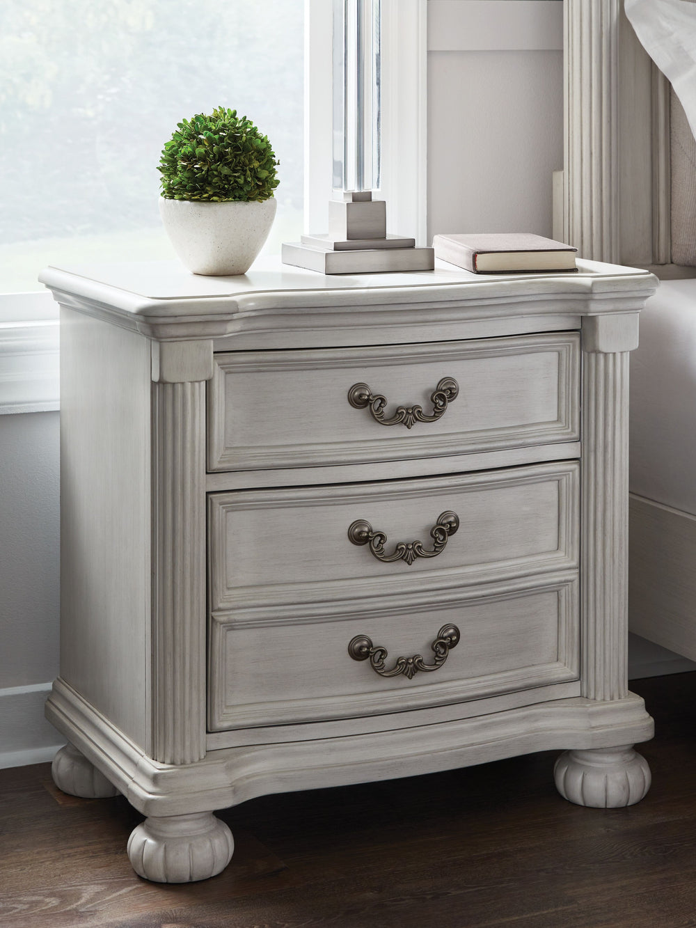 Transform your inner sanctum into a haven of timeless elegance and functionality. This traditionally styled nightstand is adorned in a classic antiqued white finish, highlighted by a serpentine-shaped front with thick decorative moulding. Its drawers are 