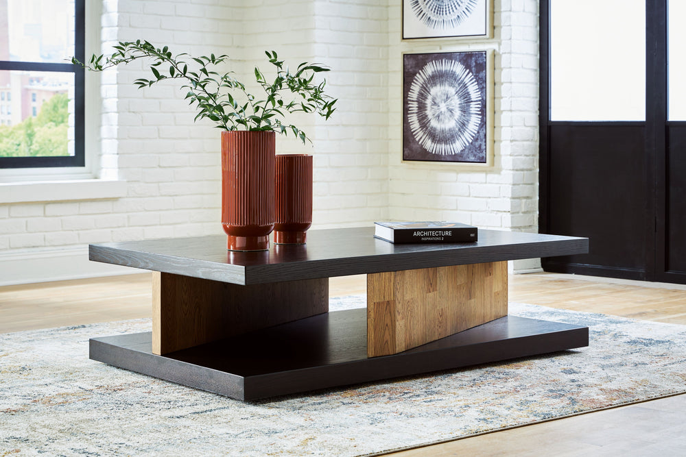 This sculptural coffee table is a perfect blend of contemporary design and relaxed living. Its clean-lined design, contrasting finish and attention-grabbing details take your decor to the next level. The cantilevered top, supported by angled plinths, adds