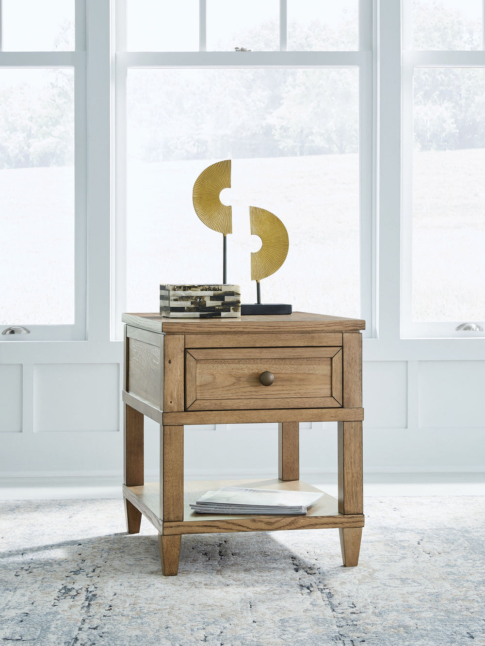 Taking a timeless approach to casual beauty, this end table brings easygoing elegance to the everyday. The light brown wood-tone finish seamlessly slips into your roomâ€™s aesthetic. A dark bronze-tone pull accents the drawer, adding to the table-'s fresh