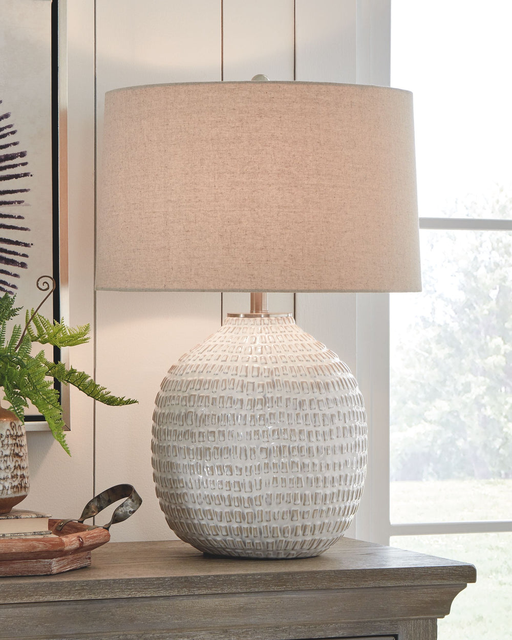 Style and function come together in this textured ceramic lamp to bring incandescent style to any space in your home. Combining a rounded base, accented with goldtone hardware, this lamp is capped off with a simple natural lampshade for complete elegance.
