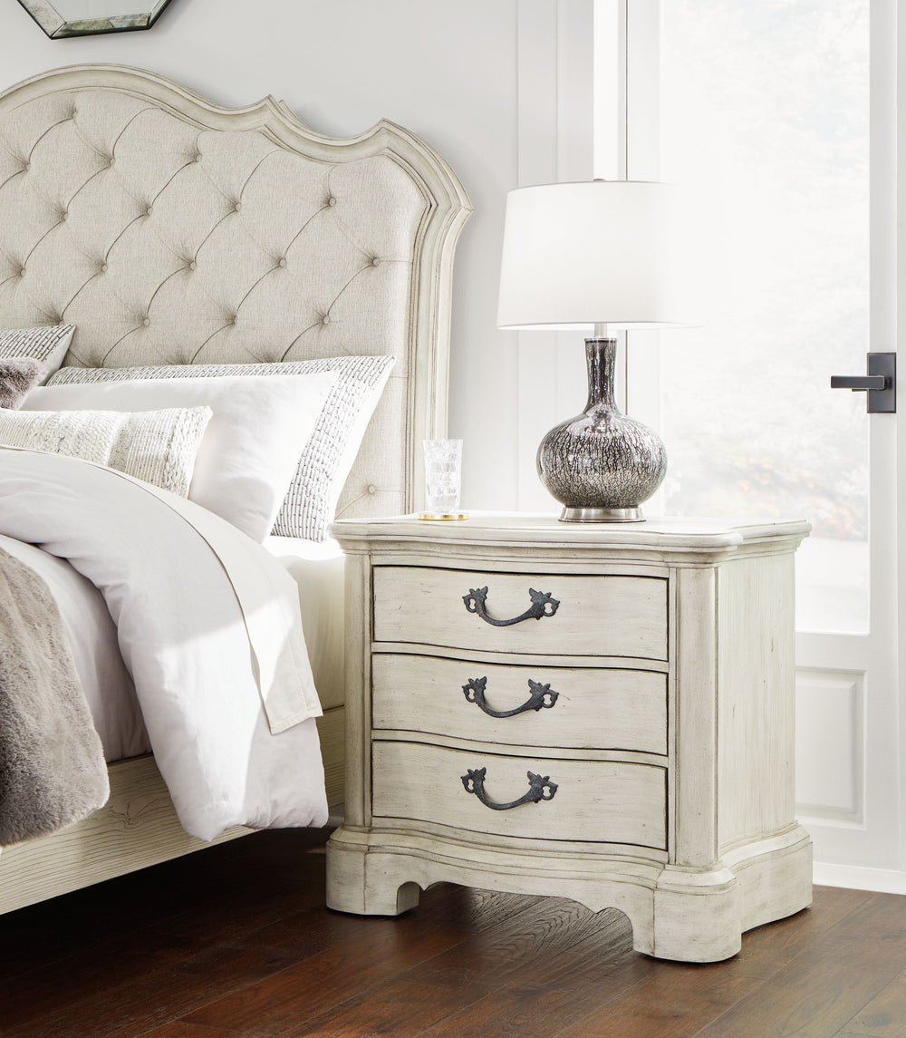 Add a touch of romance to your bedroom with this nightstand. Its antiqued white painted finish and serpentine-shaped silhouette are the definition of easy elegance. The nightstand-'s three spacious drawers accommodate bedside essentials, while an integrat