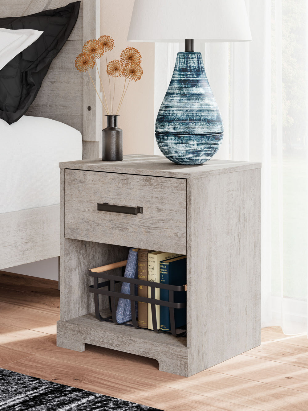 Give casual a new meaning with the chic look of this nightstand. A light gray finish over replicated oak grain keeps it laid-back and inviting, while the substantial warm pewter-tone hardware adds a modern farmhouse touch. The open cubby provides display 