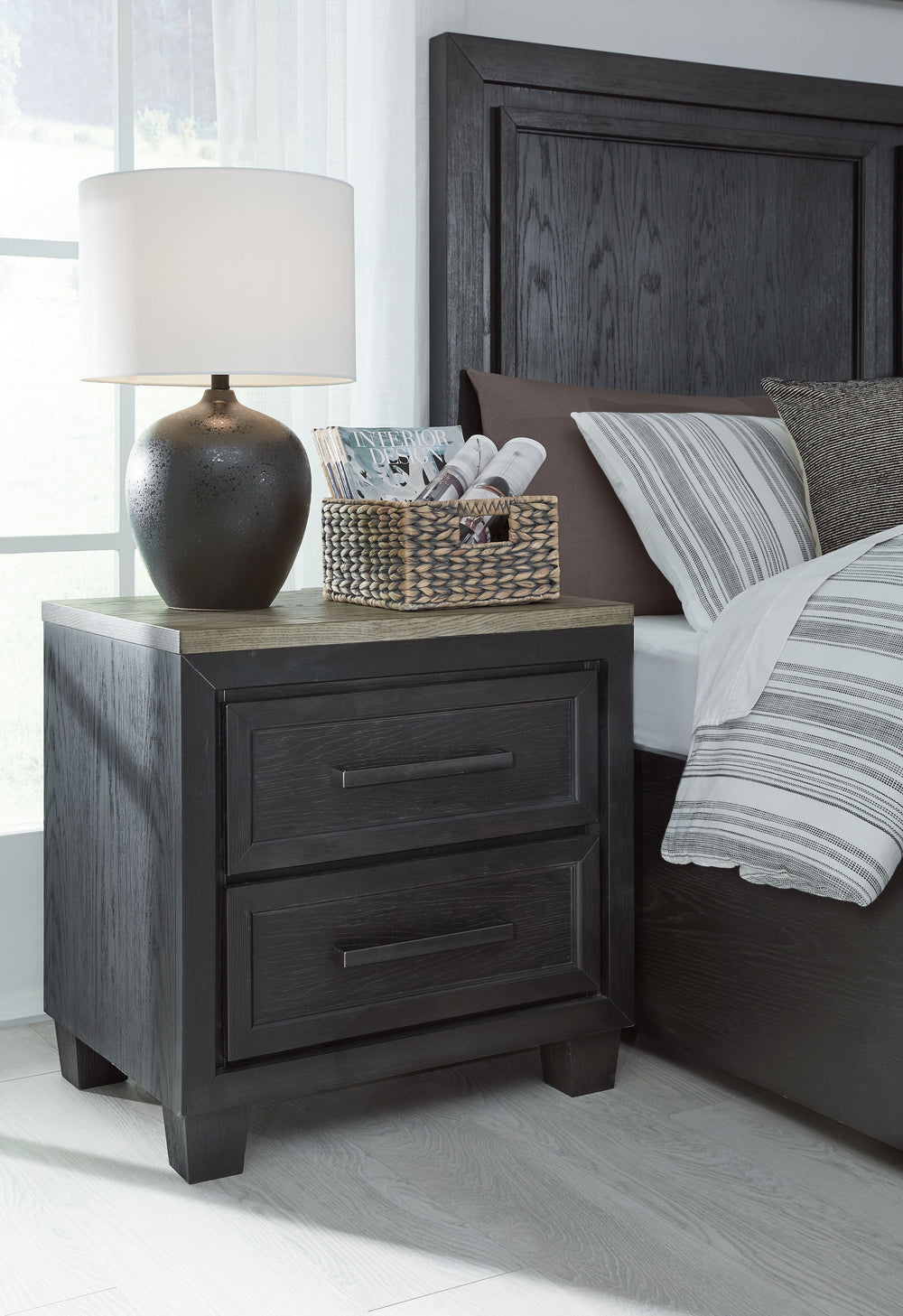 This nightstand is casual contemporary style simply done right. Its two-tone color scheme features a rich brushed black main color accented with a beautiful dusty grayish brown wood tone. Two drawers with sleek black pulls offer plenty of storage for your
