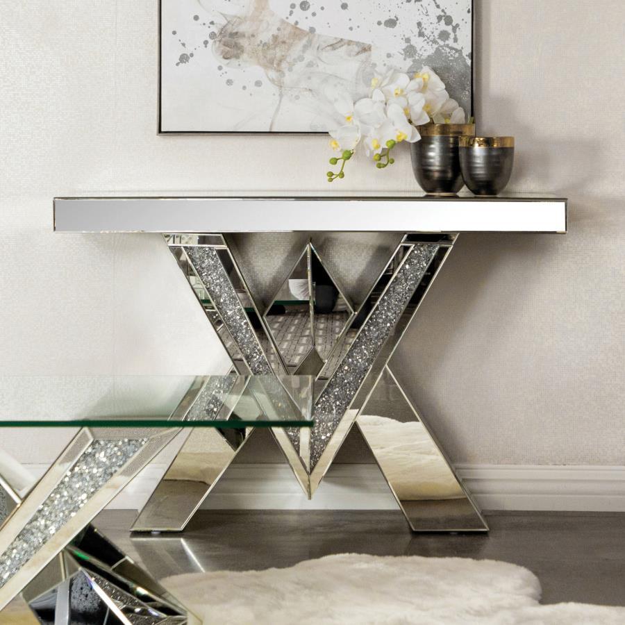 This mirrored console table boasts a striking V-shaped base with angular design elements, featuring inlays of sparkling acrylic crystals. The geometric form is complemented by sleek mirrored surfaces that enhance its modern aesthetic. The design combines 