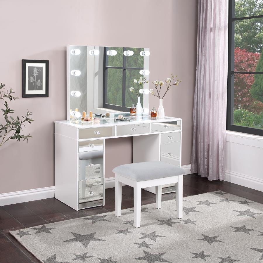 Pull out all the stops to set up a stylish and functional space for your makeup and prep, adding this three-piece white finish vanity set to a modern bedroom. Wood products construction with mirrored drawer fronts and a gray upholstered stool cushion team