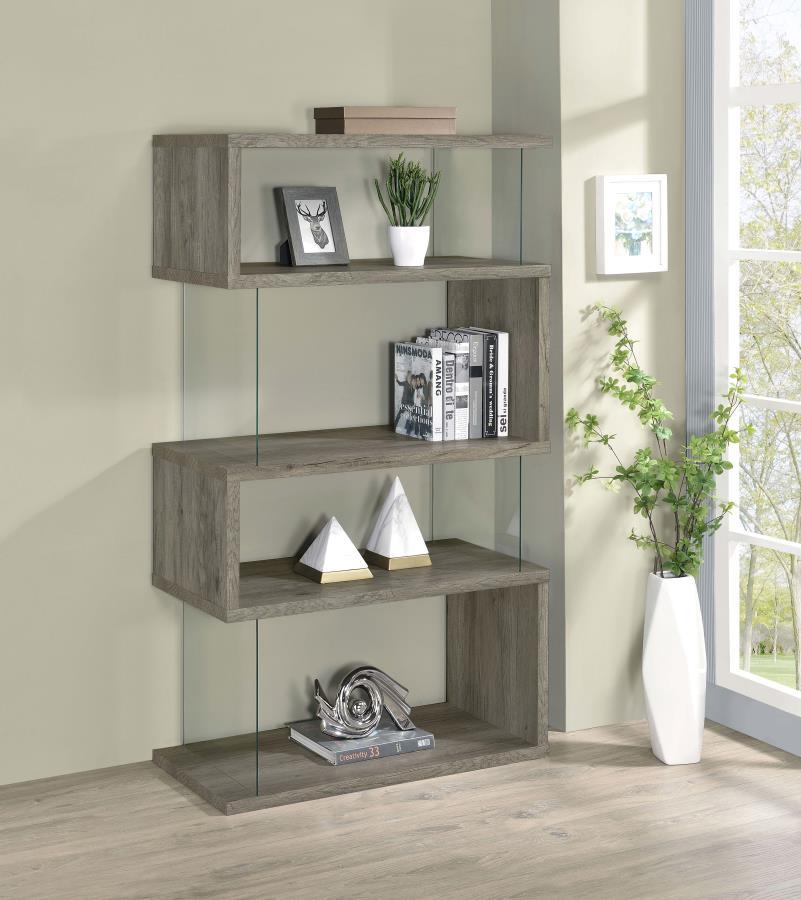 The asymmetrical zig-zag design of this contemporary bookcase creates a focal point in any room. Five open shelves in a light grey driftwood finish stack elegantly, supported by clear glass side panels that lend a modern flair to this furniture piece. Per