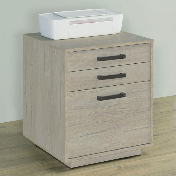  featuring a lovely whitewashed grey finish across its boxy frame and three drawers. Along each drawer is a slim gunmetal finished pull that presents an industrial modern flair to a transitional home 